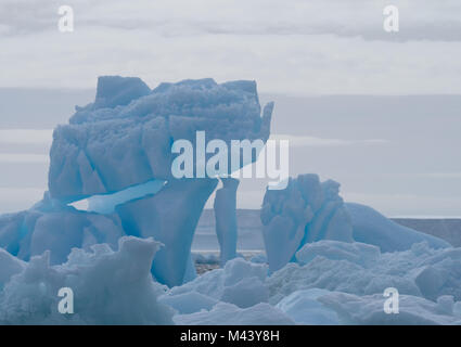 Ein hellblau Eisberg schweben in der dunkelgrauen Wasser des Südlichen Ozeans in der Antarktis. Bewölkten Himmel und Schnee Kontinent werden im Hintergrund Stockfoto