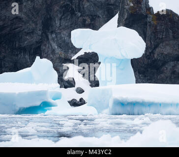 Eine ungerade Eisbildung auf ein Hellblau Eisberg mit den zerklüfteten Felsen der Antarktis im Hintergrund. In Cierva Cove fotografiert. Stockfoto