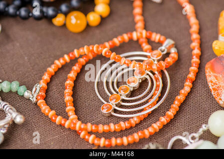 Serdolik (Karneol) Stein Kette Verlegung auf natürliche braune Bettwäsche Tischdecke. Yashma, orange Jaspis, Onyx Edelsteine herum. Heilung, kraftvolle Energie f Stockfoto