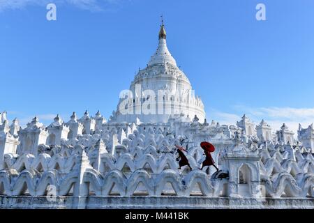 Die buddhistischen Kinder mit roten Bademäntel und Schirme in einem weißen Buddha Tempel mit blauer Skyline läuft Stockfoto