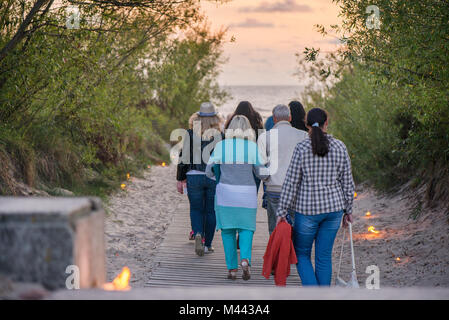 Romantische Lagerfeuer Nacht am Meer bei Sonnenuntergang. Leute versammeln um Nacht der alten Leuchten feiern. Wandern auf Holz weg Stockfoto