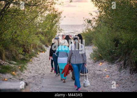 Romantische Lagerfeuer Nacht am Meer bei Sonnenuntergang. Leute versammeln um Nacht der alten Leuchten feiern. Wandern auf Holz weg Stockfoto