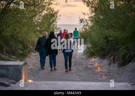 Romantische Lagerfeuer Nacht am Meer bei Sonnenuntergang. Leute versammeln um Nacht der alten Leuchten feiern. Wandern auf Holz weg Stockfoto