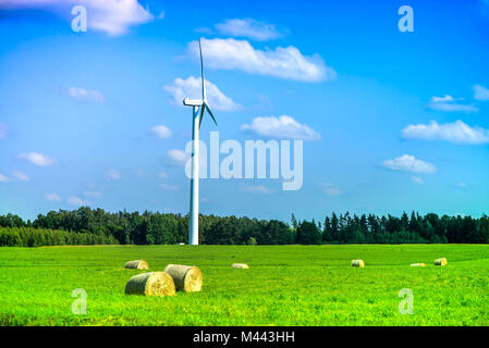 Szene Sommer wind turbine in der Mitte der Wiese voller Strohballen, neben Wald, während der schönen Sonnenuntergang auf Land. Ländliche Landschaft, wi Stockfoto