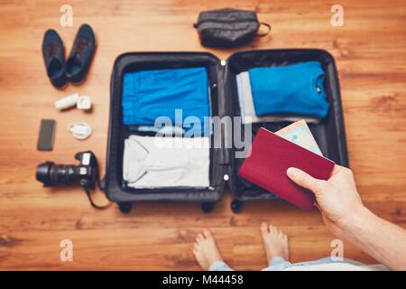 Vorbereitung Gepäck für die Reise. Junger Mann Verpackung Ferienhäuser Reihen: Kleidung, Handy, Kamera und Reisepass mit Geld. Stockfoto