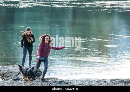 Zwei junge Frauen laufen mit Hund von Fluss, Calolziocorte, Lombardei, Italien Stockfoto