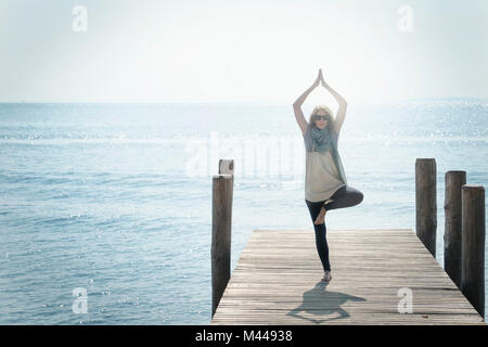 Frau auf Pier auf ein Bein im Yoga pose Stockfoto