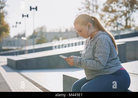 Kurvenreiche junge Frau Ausbildung, sitzen auf der Wand auf Smartphone Stockfoto