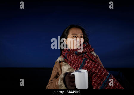 Junge Frau in Schal gewickelt am Strand bei Nacht, Tarragona, Katalonien, Spanien Stockfoto
