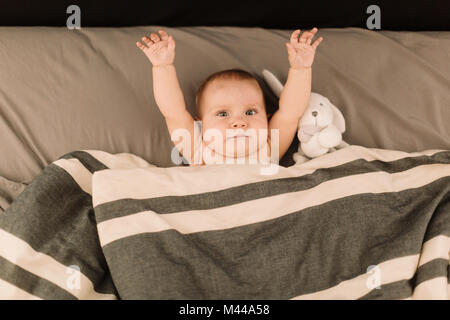 Portrait von baby girl im Bett lag, mit erhobenen Armen, Ansicht von oben Stockfoto