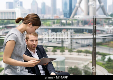 Junge Geschäftsfrau und Mann an digitalen Tablet auf Sidewalk Cafe in Shanghai Financial Center, Shanghai, China Stockfoto