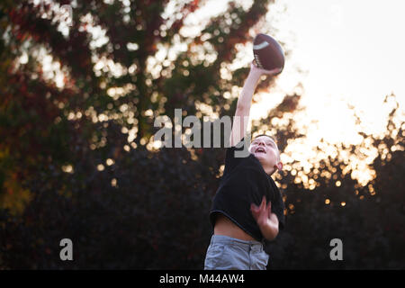 Junge praktizierende American Football in Garten erreichen Ball zu fangen Stockfoto