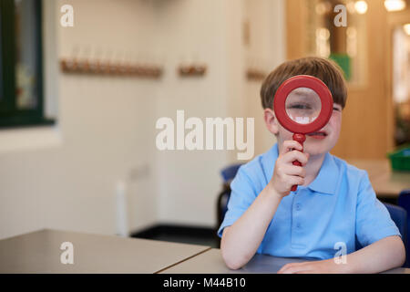 Schüler durch die Lupe im Unterricht in der Grundschule suchen, Porträt Stockfoto