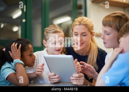 Lehrer mit Schüler und Schülerinnen bei Digital tablet Suchen im Unterricht in der Grundschule Stockfoto