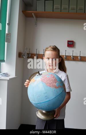 Schulmädchen holding Globe im Unterricht in der Grundschule, Porträt Stockfoto