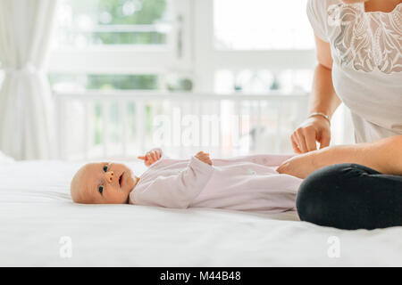 Junge Frau Dressing baby Tochter auf dem Bett, 7/8 Stockfoto