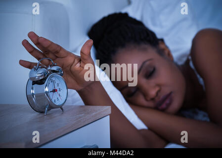 Frau schlafend auf dem Bett Ausschalten der Wecker Stockfoto