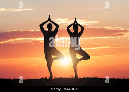 Silhouette von Paar Yoga Gegen dramatische Himmel bei Sonnenuntergang Stockfoto