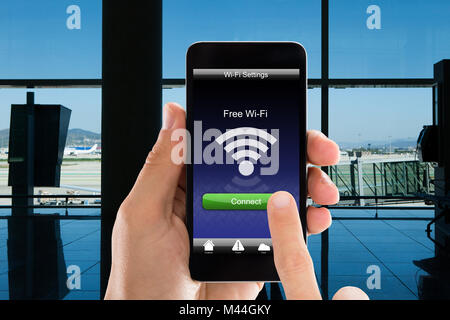 Zugeschnittenes Bild der Person über Wlan auf smart phone in Flughafen Stockfoto