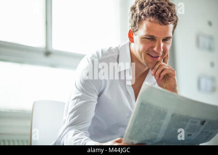 Hübscher junger Geschäftsmann lesen Zeitung im Büro Stockfoto