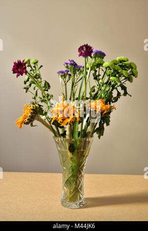 Ein Bündel von sterbenden Blumen in einer Glasvase. Stockfoto