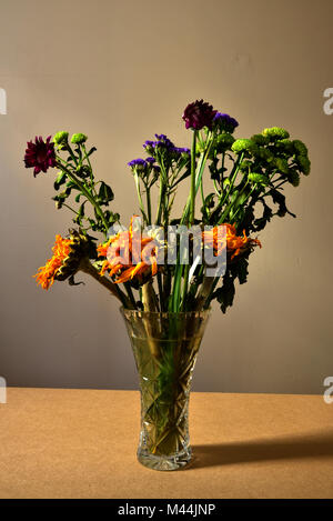 Ein Bündel von sterbenden Blumen in einer Glasvase. Stockfoto