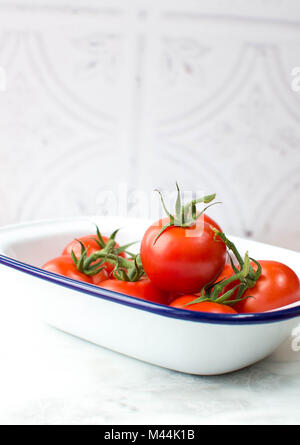 Leuchtend rote Tomaten in eine Schüssel mit weißen Negative füllen. Rohstoff, helles Rot mit Blau und Weiß Emaille Teller in auf einem weißen Marmor Oberfläche geschossen. Stockfoto