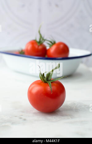 Leuchtend rote Tomaten in eine Schüssel mit weißen Negative füllen. Rohstoff, helles Rot mit Blau und Weiß Emaille Teller in auf einem weißen Marmor Oberfläche geschossen. Stockfoto