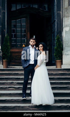 In voller Länge Hochzeit schoss der schönen jungen jungvermählte Paar auf der Treppe der alten Kirche posieren. Stockfoto