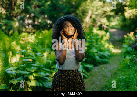 Nahaufnahme Porträt der charmanten friedlichen afrikanischen Mädchen mit grünen Lippenstift und Lidschatten setzen Sie die Ohrhörer an den grünen verschwommenen Hintergrund. Stockfoto