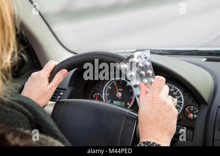 Hände mit Packs von Tabletten am Lenkrad eines Autos während der Fahrt Stockfoto