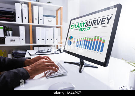 Nahaufnahme der Kaufmann Hand Analyse Gehalt Umfrageergebnisse auf Computer am Arbeitsplatz Stockfoto