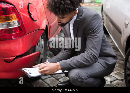 Junge männliche Insurance Agent Schreiben auf Zwischenablage während der Prüfung beschädigt roten Auto Stockfoto