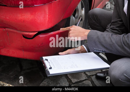 Junge männliche Insurance Agent Schreiben auf Zwischenablage während der Prüfung beschädigt roten Auto Stockfoto