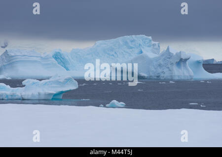 Blauer Eisberg floating im Südlichen Ozean mit einer dichten Wolke bank mit dunkelgrauen Wolken Overhead und einem weißen Schnee im Vordergrund. Stockfoto