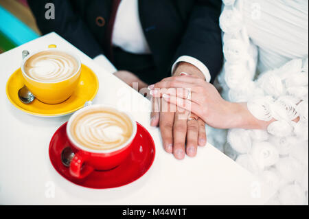 Tabelle mit zwei gelbe und rote Tassen Kaffee, Cappuccino. Paar, Braut und Bräutigam, Hände auf den Tisch. Liebe, Hochzeit Konzept. Stockfoto