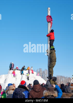 Nowosibirsk, Russland - Januar 11, 2018: Junge klettern auf eine hölzerne Stange für den Preis. Slawische Volksmusik Festlichkeiten oder Fastnacht Maslenitsa. Historische ein Stockfoto