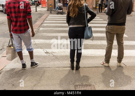 Eine Ansicht der Rückseite drei junge Leute stehen auf der Straße warten die Straße an einem fußgängerüberweg in der Stadt Bologna Italien überqueren Stockfoto