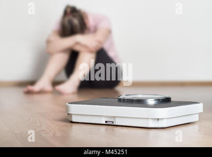 Gewicht-Verlust-Fail-Konzept. Skala und deprimiert, frustriert und traurig Frau Stock hält Kopf und Arme auf Knien sitzen. Stockfoto