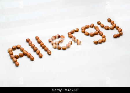 Allergie mit Erdnüssen geschrieben. Wort und Text aus Nüssen. Erdnüsse auf weissem Holztisch oder Board. Allergische Reaktion und Ernährung problem Konzept Stockfoto