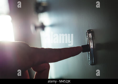 Finger, mit türklingel in Gang. Nahaufnahme der männlichen Hand läutenden Türglocke in einem Mehrfamilienhaus. Unerwünschte Gäste, schlechte Nachrichten. Stockfoto