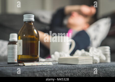 Kranke Frau mit Kopf und Stirn mit der Hand und des Arms. Medizin, Thermometer, heißes Getränk und verschmutzte Papierhandtücher in Front. Person mit Grippe. Stockfoto