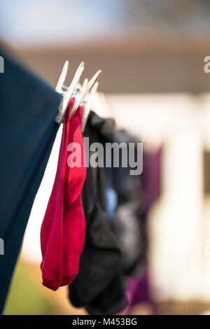 Rote Socken und Kleiderpeisten aus der Nähe, die an der Wäscheleine im Garten hängen und bei Wind trocknen. Stockfoto