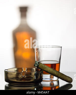 Whiskey, ein Aschenbecher und eine rauchen Zigarre auf dem Hintergrund einer Flasche Stockfoto