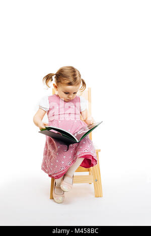 Kleinkind Mädchen das Lesen eines Buches auf einem Stuhl sitzend, weißer Hintergrund Stockfoto