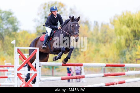 Junge Reiter Mädchen auf Bay Horse über Barriere auf Pferdesport Wettbewerb springen. Reiten, Mädchen auf Show Jumping Wettbewerb Stockfoto