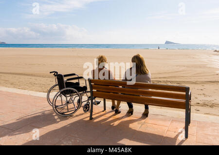 Frau auf der Bank sitzen und auf das Meer. Für Rollstuhlfahrer stehen in der Nähe von Ihnen Stockfoto