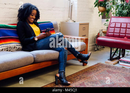 Frau sitzt auf einem Sofa von SMS-Nachrichten auf dem Smartphone lächelnd Stockfoto
