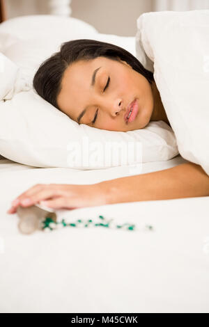 Brünette im Bett durch verschüttete Flasche Pillen Stockfoto