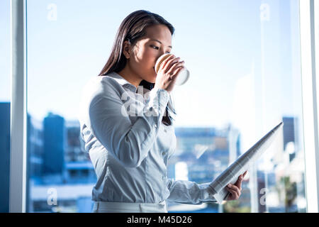 Lächelnd Geschäftsfrau holding Einweg-Schale lesen Zeitung Stockfoto